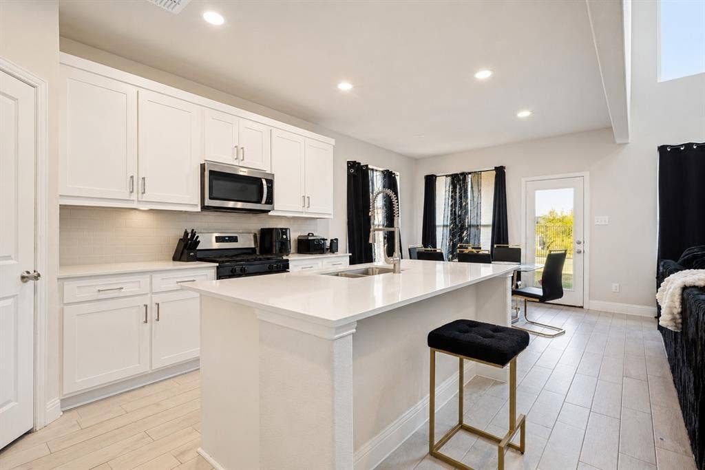 2902 Cremini Fls, Princeton, TX 75407 Kitchen featuring white shaker-style cabinetry, stainless steel appliances, a center island with sink, and light-toned wood-finish flooring