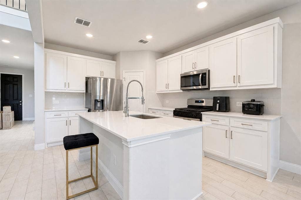 2902 Cremini Fls, Princeton, TX 75407 Kitchen featuring a central island, white cabinetry, integrated stainless-steel appliances, subway tile backsplash, and light wood-finish flooring