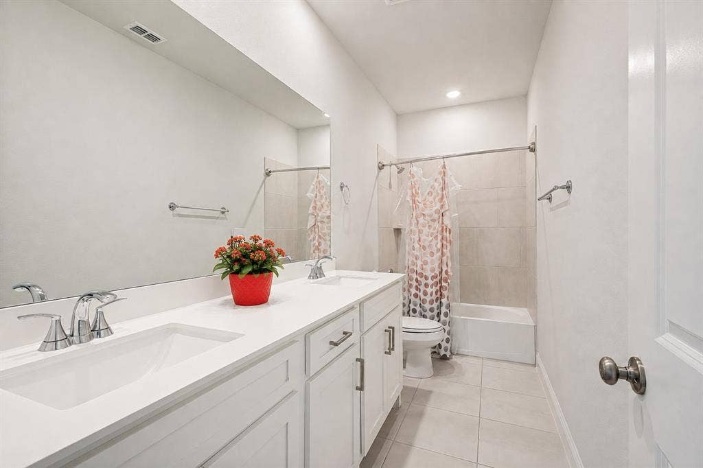 2902 Cremini Fls, Princeton, TX 75407 Dual vanity with chrome fixtures and integrated sinks, a full-width mirror, light-toned floor tiling, and a bathtub with a tiled surround
