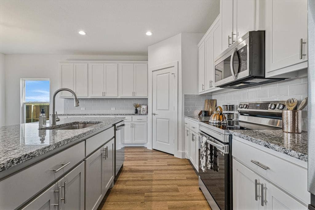 Kitchen featuring an island with an undermount sink, stainless steel appliances, granite countertops, white cabinetry, and wood-finish flooring