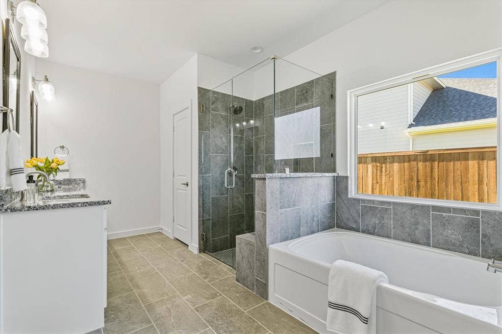 Dual vanity with granite countertops, a walk-in shower with glass enclosure, a built-in soaking tub, and neutral-toned tile flooring