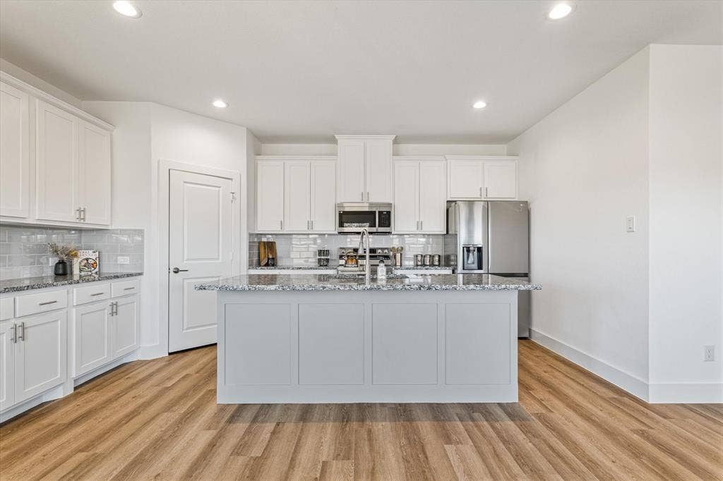 Bright kitchen featuring an expansive center island with stone countertop, wood-finish flooring, white cabinetry, and stainless steel appliances