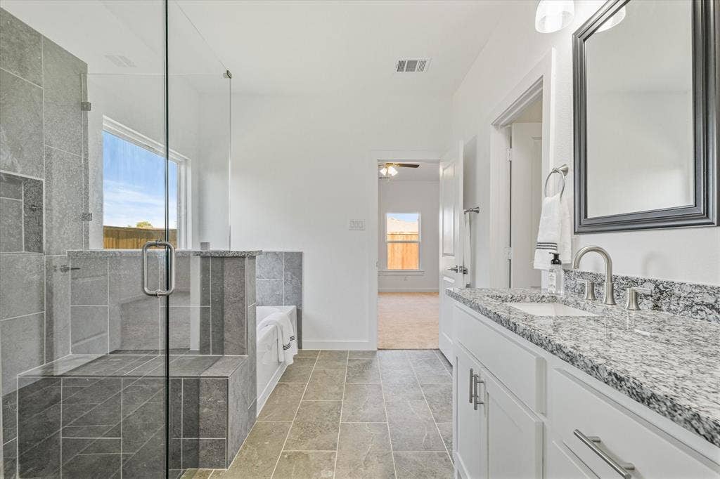 Spacious bathroom featuring a glass-enclosed shower with a built-in bench, a separate soaking tub, a dual vanity with a granite countertop, and tiled flooring