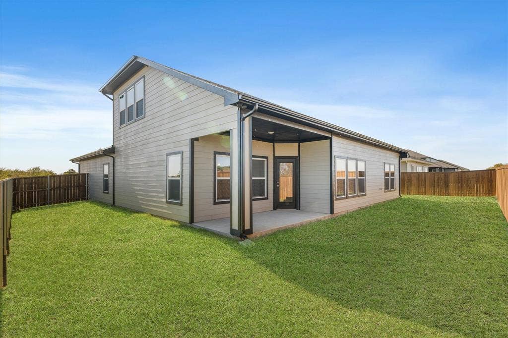 Expansive backyard featuring a covered patio, wood-tone fencing, and a manicured lawn