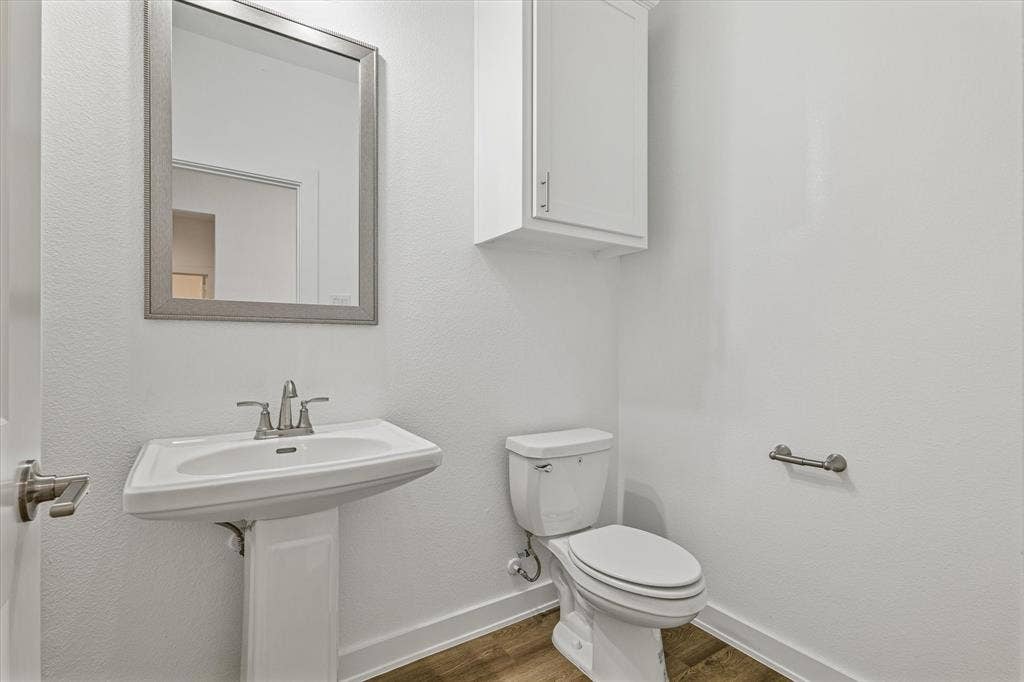 Pedestal sink with a chrome faucet, wall-mounted mirror, white toilet, and wood-finish flooring