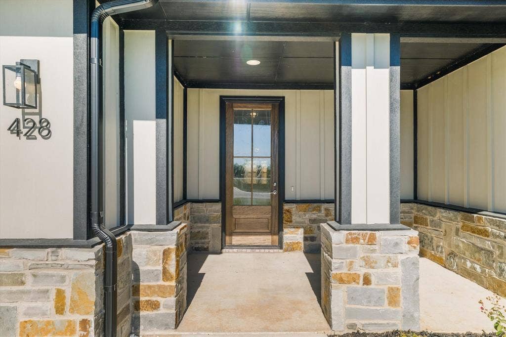 Stone accent facade with board and batten siding, dark wood-finish entry door with glass panels, and a concrete porch