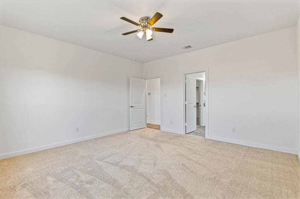 Spacious room featuring neutral carpeting, white walls, and a ceiling fan with integrated lighting