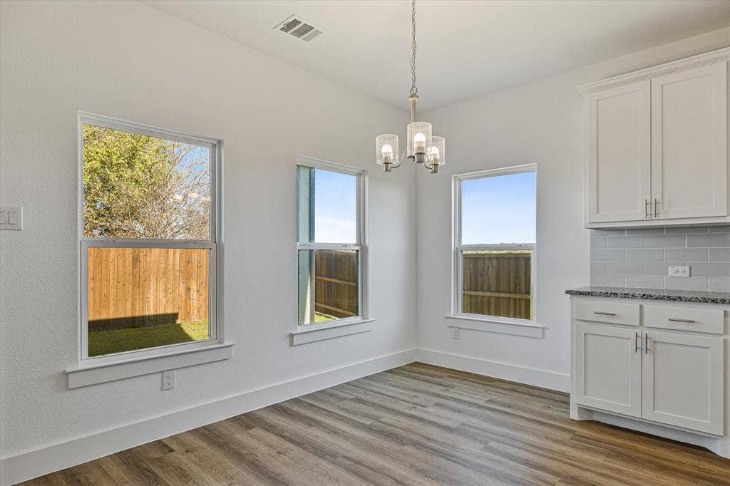 Wood-finish flooring with white baseboards, multiple windows, and a chandelier with glass shades