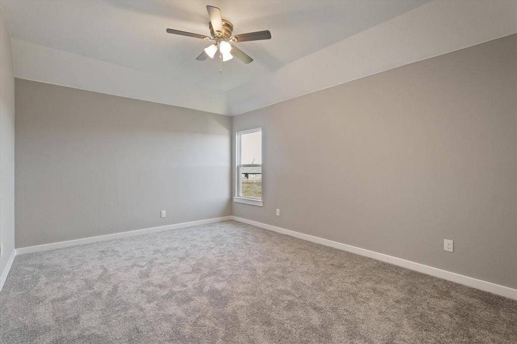 Tray ceiling, ceiling fan with integrated lighting, window with white trim, light gray carpet flooring, and neutral wall paint
