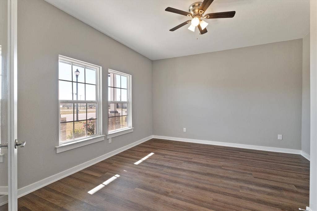 Wood-finish flooring, dual windows with grid patterns, light gray wall finish, and a ceiling fan with integrated lighting