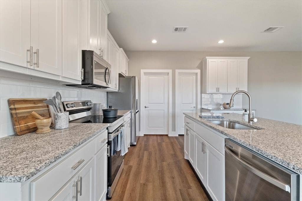 Kitchen featuring white cabinetry, gray speckled countertops, stainless steel appliances, wood-finish flooring, and a white subway tile backsplash