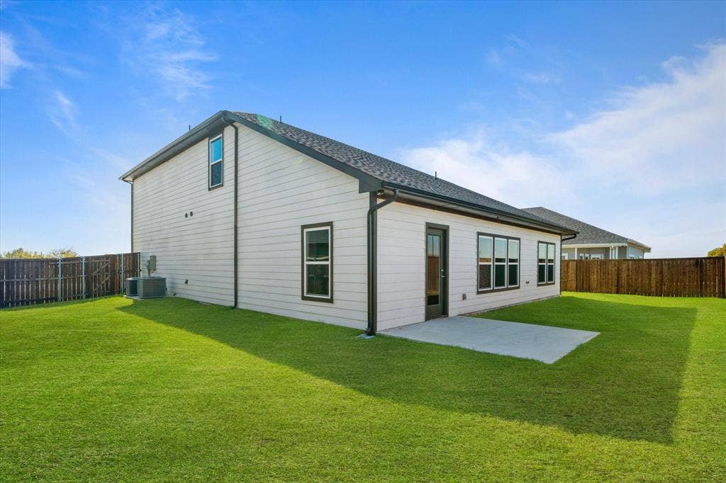 Expansive backyard featuring a manicured lawn, concrete patio, and dark wood-finish fencing
