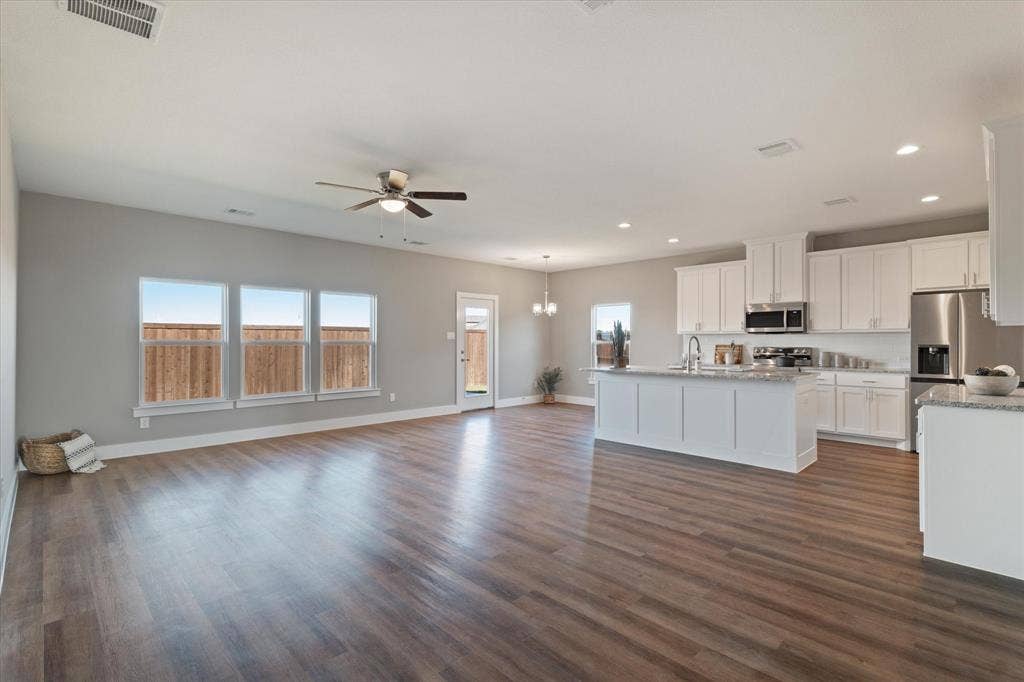 Open-concept living area with wood-finish flooring, white cabinetry, stainless steel appliances, and a kitchen island with a sink