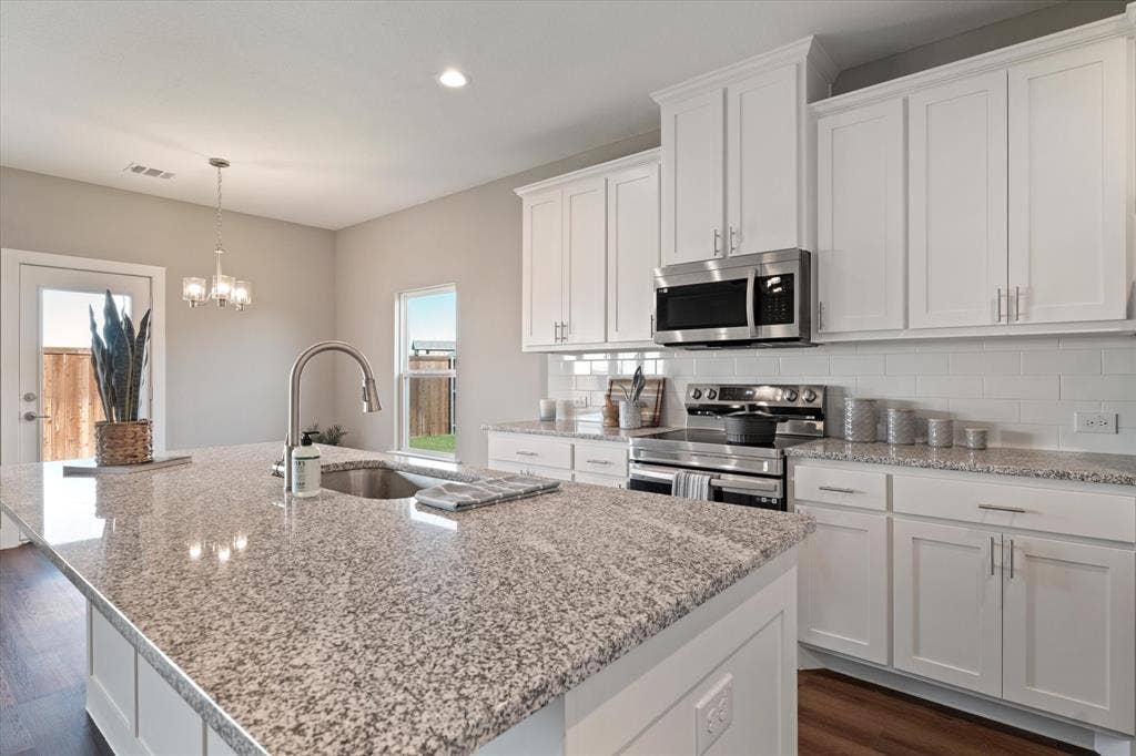 Kitchen featuring a large island with an undermount sink, stainless steel appliances, white cabinetry with silver hardware, and subway tile backsplash