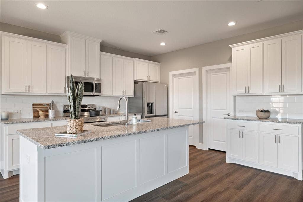 White shaker-style cabinetry, stainless steel appliances, granite countertops, subway tile backsplash, and wood-finish flooring