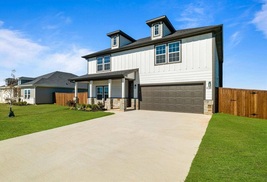 Two-story exterior with dormer windows, covered front porch, stone column accents, and an attached two-car garage