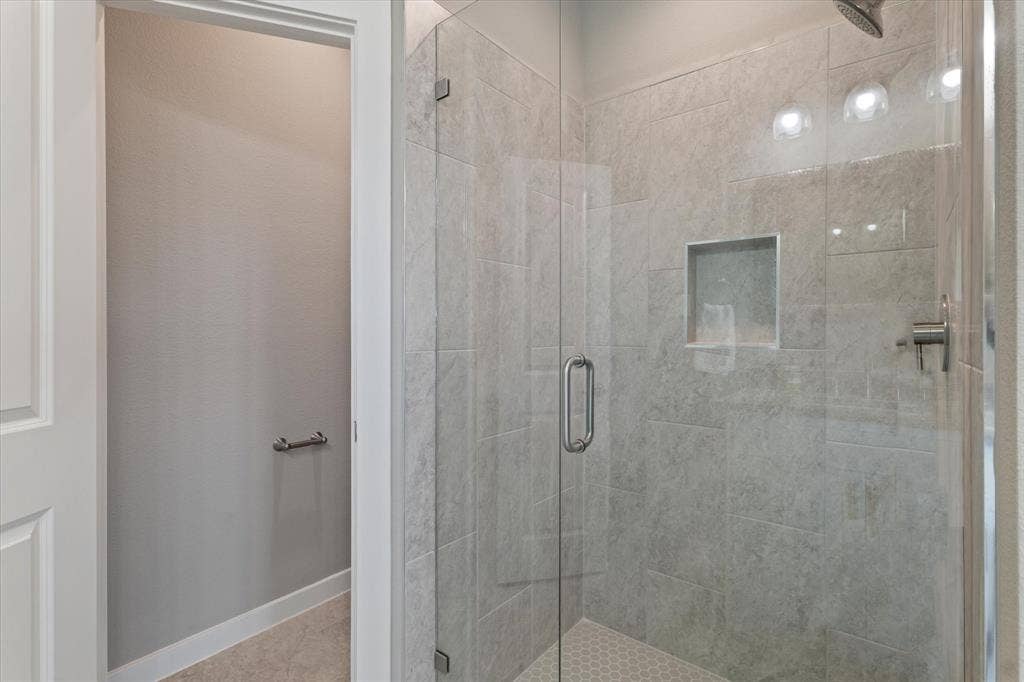 Glass-enclosed shower with a recessed shelf, tile surround, and hexagonal tile flooring