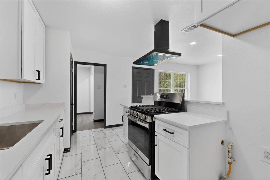 301 Stoneport Drive, Dallas, TX 75217 Kitchen featuring white cabinetry, light-toned countertops, a stainless steel gas range, a black range hood, and large format tile flooring
