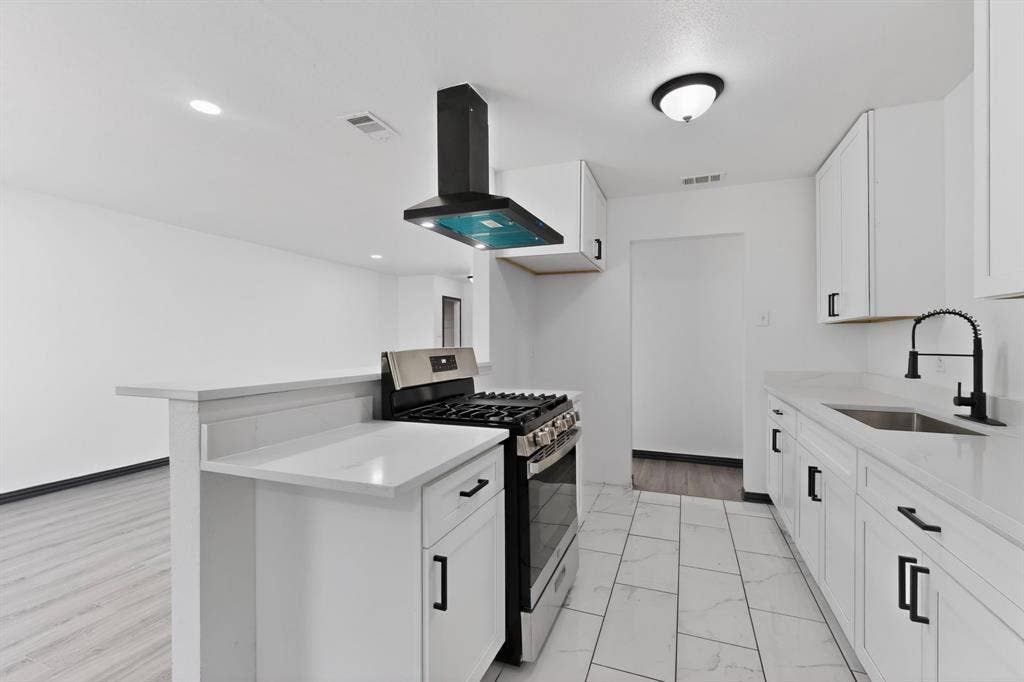 301 Stoneport Drive, Dallas, TX 75217 Kitchen featuring white cabinetry, light-toned countertops, a stainless steel range with a black vent hood, and white tile flooring