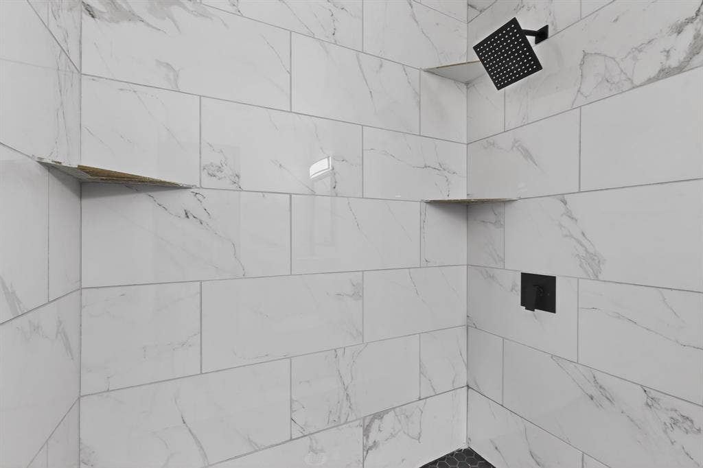 301 Stoneport Drive, Dallas, TX 75217 Shower enclosure featuring white marble-look subway tiles, a matte black rain shower head, matte black shower controls, two built-in corner shelves, and a black hexagon tile floor