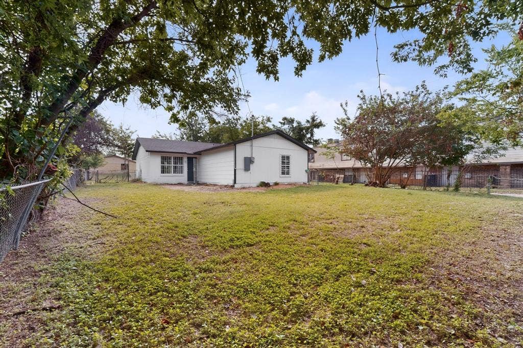 301 Stoneport Drive, Dallas, TX 75217 Expansive backyard featuring a chain-link fence, mature trees, and a white siding exterior