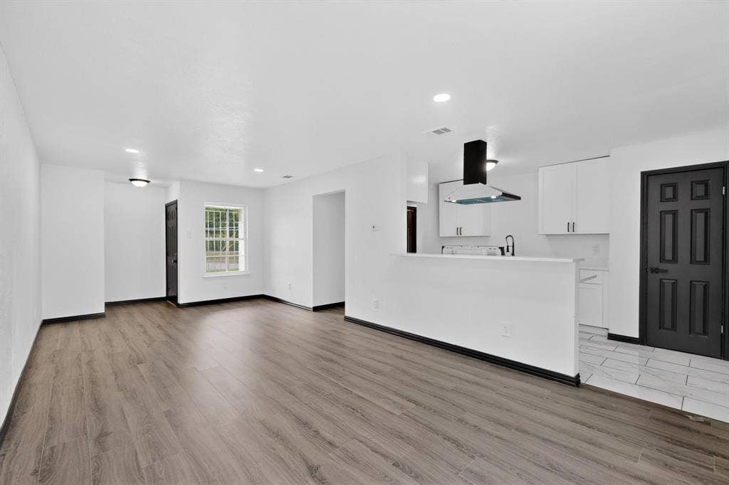 301 Stoneport Drive, Dallas, TX 75217 Open-concept living area with wood-finish flooring, recessed lighting, and a kitchen featuring white cabinetry, a kitchen island, and a stainless steel range hood