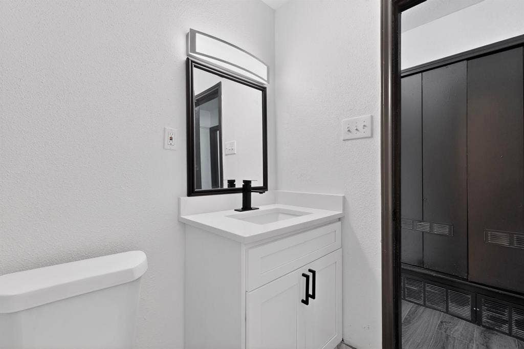 301 Stoneport Drive, Dallas, TX 75217 White vanity with integrated sink and matte black faucet, framed mirror with overhead lighting, and wood-finish flooring