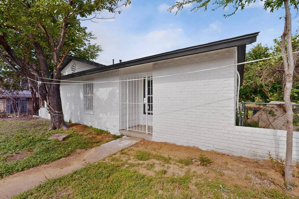 301 Stoneport Drive, Dallas, TX 75217 White painted brick exterior with black trim, a security screen door, and a partially fenced yard