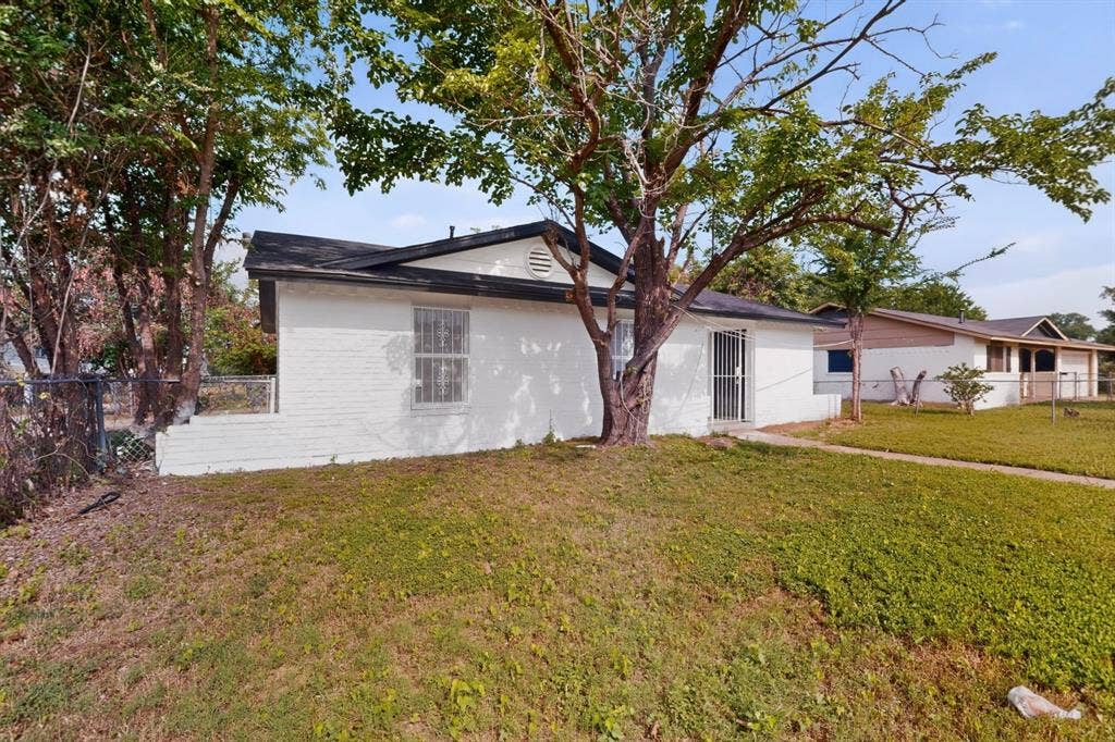 301 Stoneport Drive, Dallas, TX 75217 White brick exterior with a black shingle roof, featuring a security screen door and a fenced side yard