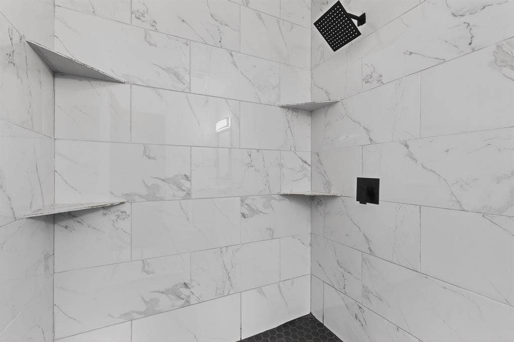 301 Stoneport Drive, Dallas, TX 75217 Shower featuring white rectangular tile with subtle veining, dual built-in corner shelves, a matte black shower head, and a matte black wall-mounted control
