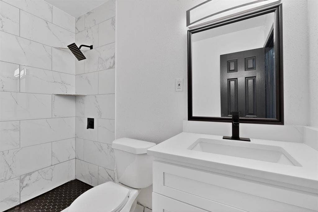 301 Stoneport Drive, Dallas, TX 75217 Modern bathroom featuring a vanity with integrated sink, a rectangular framed mirror, and a shower with tile surround and black hexagonal floor tile