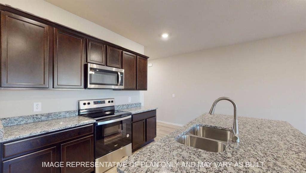 10405 Altair Drive, Waco, TX 76708 Dark wood-finish cabinetry, stainless steel appliances, speckled stone countertops, and an undermount double basin sink with a high-arc faucet