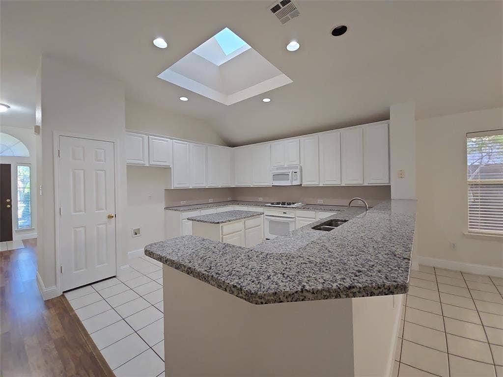 2424 Brycewood Lane, Plano, TX 75025 Kitchen featuring white cabinetry, granite countertops, tile flooring, a built-in microwave, and a skylight