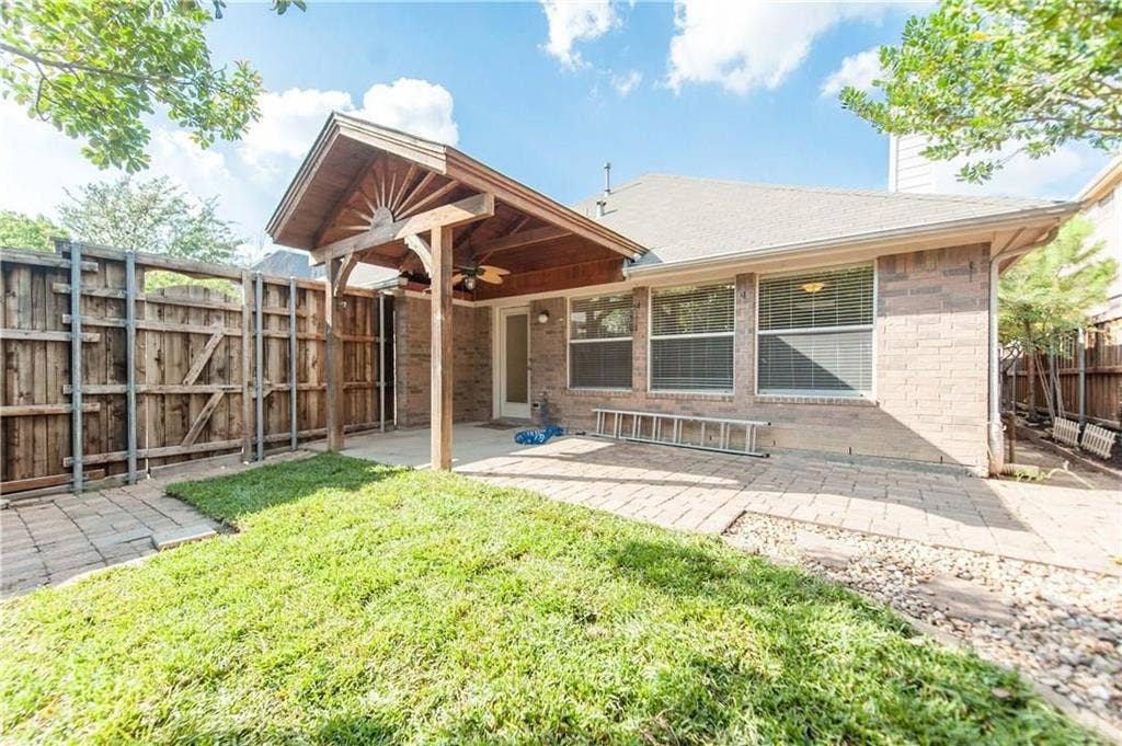2424 Brycewood Lane, Plano, TX 75025 Brick exterior with multiple windows, covered patio featuring a ceiling fan, paved patio area, and a wood privacy fence