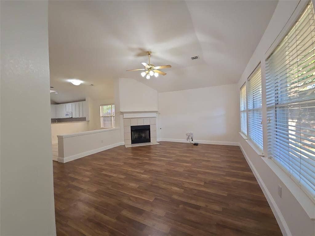 2424 Brycewood Lane, Plano, TX 75025 Vaulted ceiling with a ceiling fan, wood-finish flooring, and a fireplace with a tile surround and mantel
