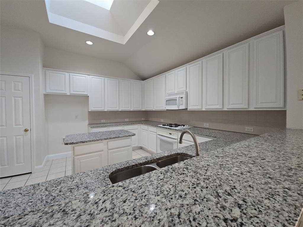 2424 Brycewood Lane, Plano, TX 75025 Spacious kitchen featuring extensive granite countertops, white cabinetry, a skylight, recessed lighting, and a center island