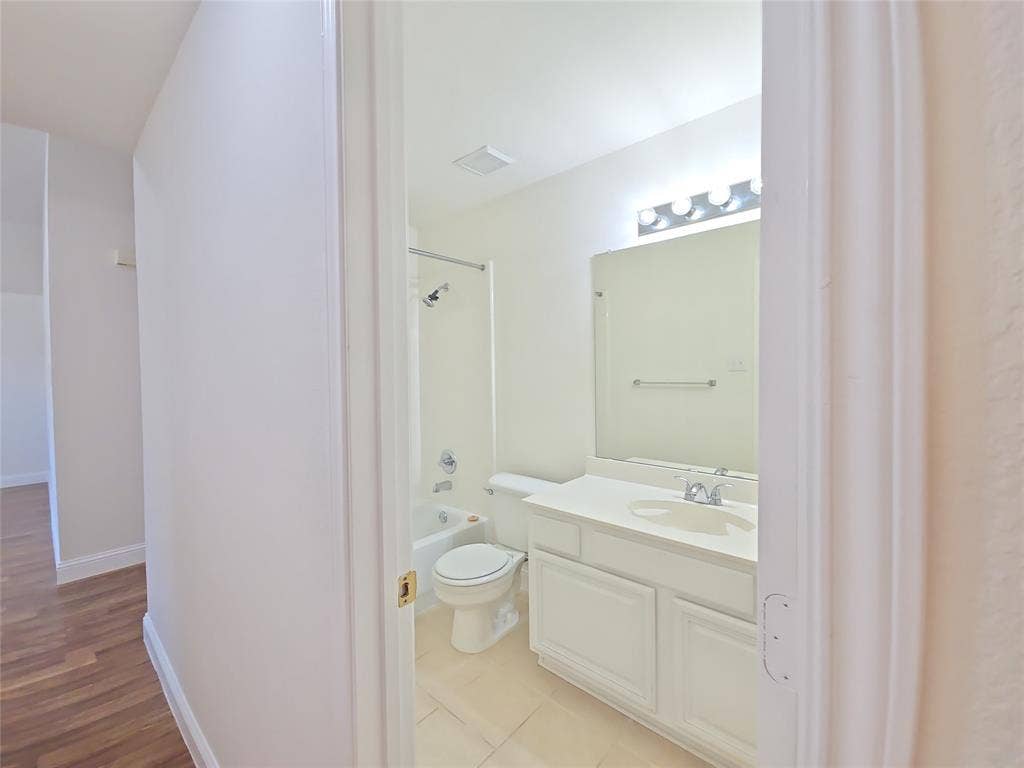 2424 Brycewood Lane, Plano, TX 75025 Bathroom featuring a single-sink vanity with white cabinetry, a built-in bathtub with shower, and tiled flooring