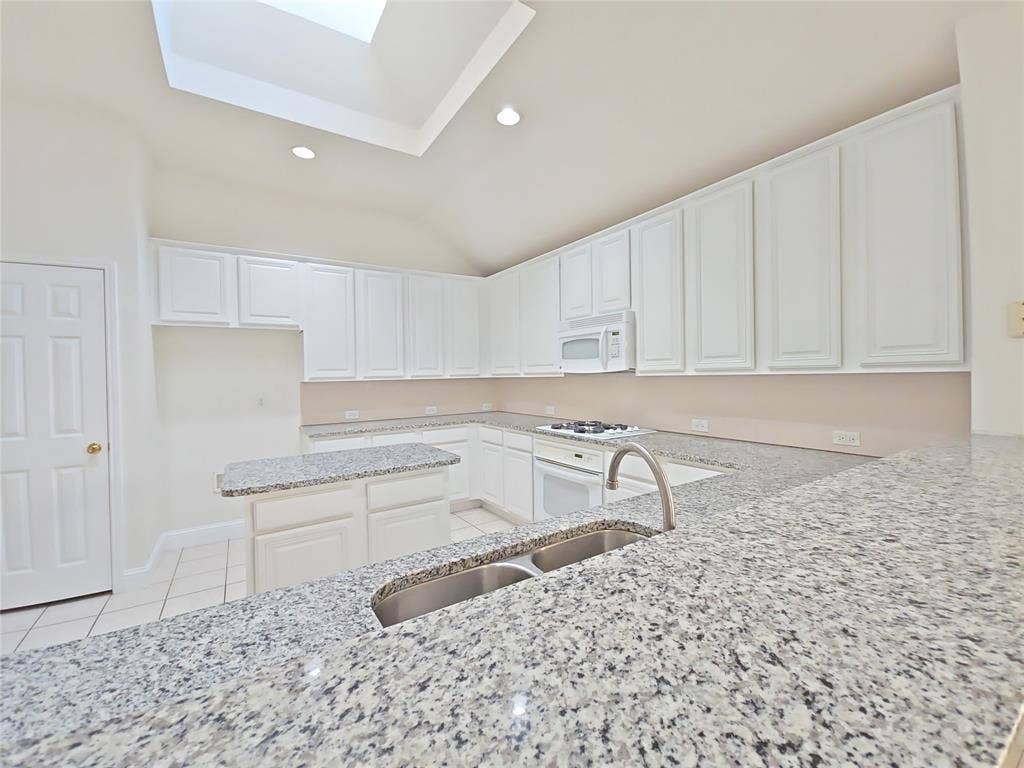 2424 Brycewood Lane, Plano, TX 75025 Kitchen featuring granite countertops, white cabinetry, a dual basin stainless steel sink, and a skylight