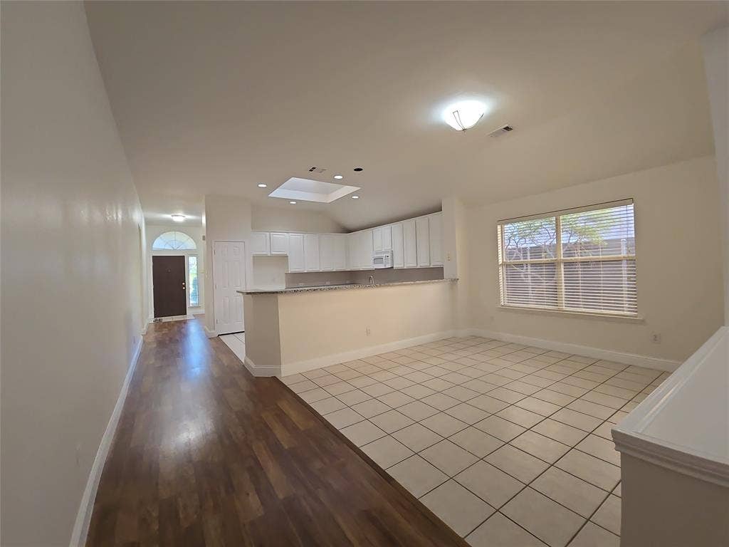 2424 Brycewood Lane, Plano, TX 75025 Combined flooring surfaces, vaulted ceiling, kitchen pass-through, skylight, and window with horizontal blinds