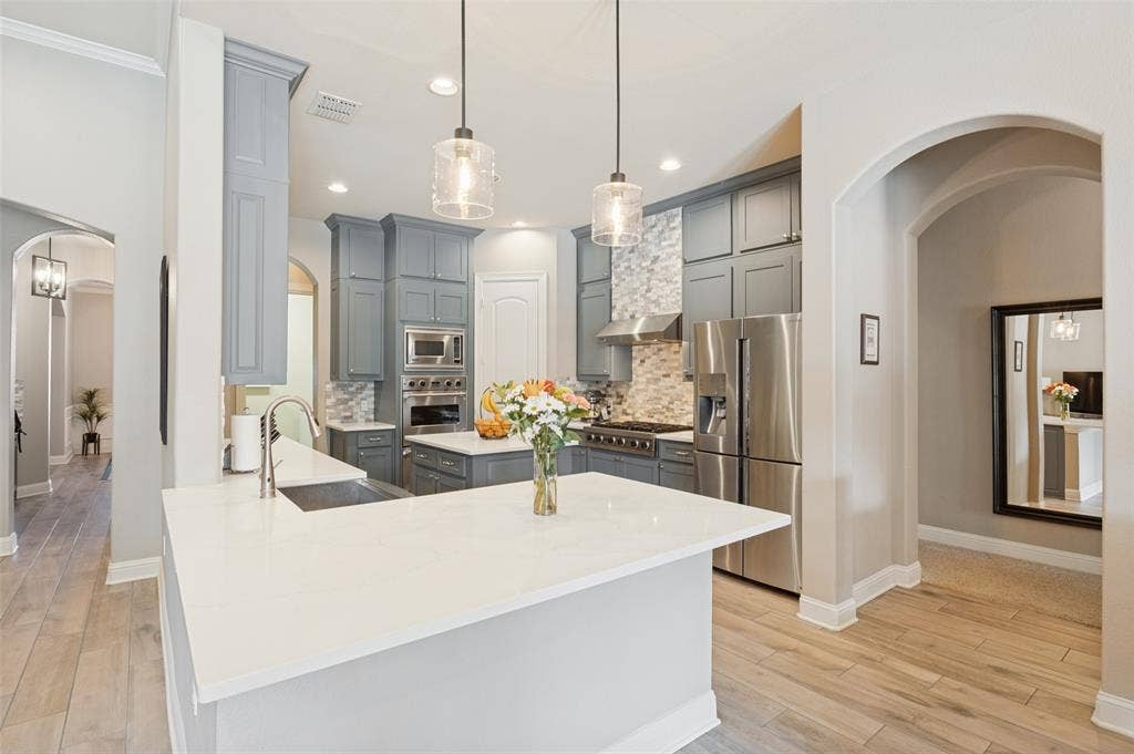 1504 Daisy Lane, Flower Mound, TX 75028 Kitchen featuring light grey cabinetry, stainless steel appliances, a white island, contemporary pendant lighting, and wood-finish flooring