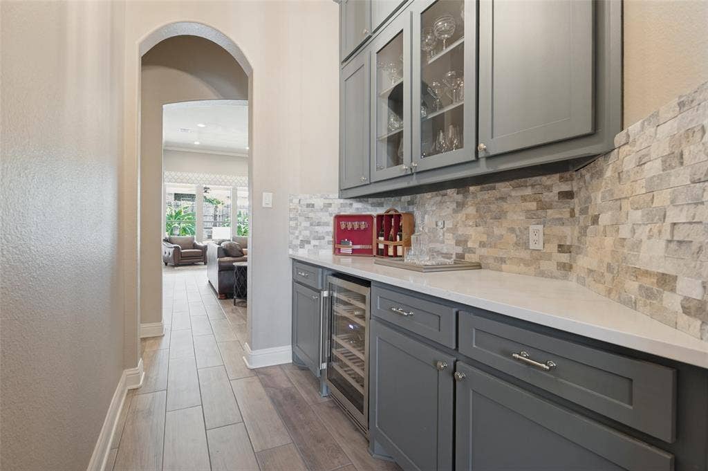 1504 Daisy Lane, Flower Mound, TX 75028 Custom built-in cabinetry with glass-front uppers, solid surface countertop, stacked stone backsplash, and integrated beverage refrigerators