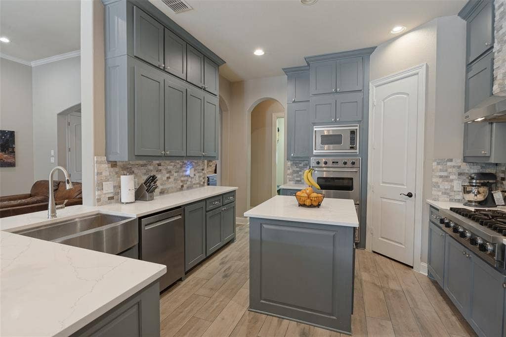 1504 Daisy Lane, Flower Mound, TX 75028 Spacious kitchen featuring gray shaker-style cabinetry, a central island, stainless steel appliances, and wood-finish flooring