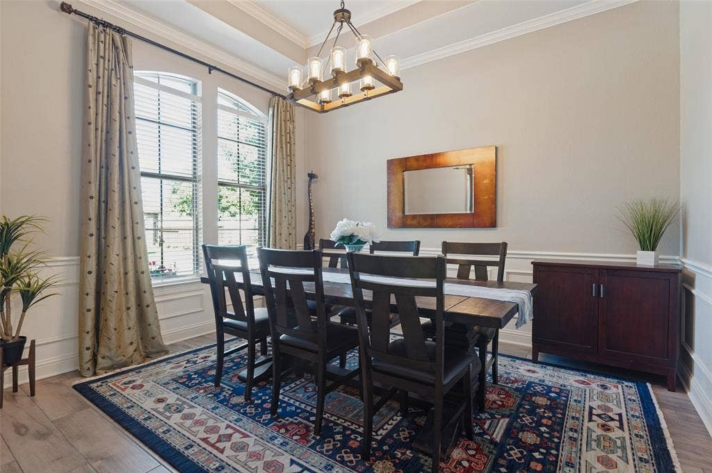1504 Daisy Lane, Flower Mound, TX 75028 Tray ceiling with crown molding, decorative chandelier, arched windows with blinds, wainscoting, and wood-finish flooring