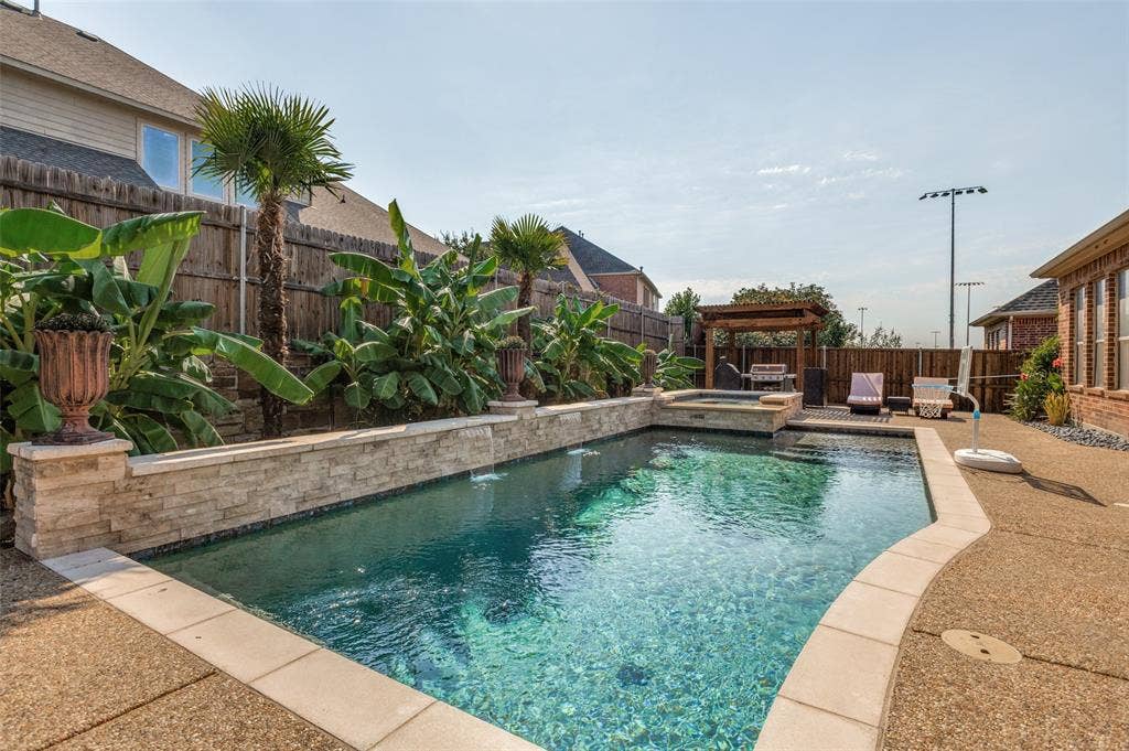 1504 Daisy Lane, Flower Mound, TX 75028 In-ground pool with stone coping, integrated spa, and a flagstone-clad raised planter with mature tropical landscaping