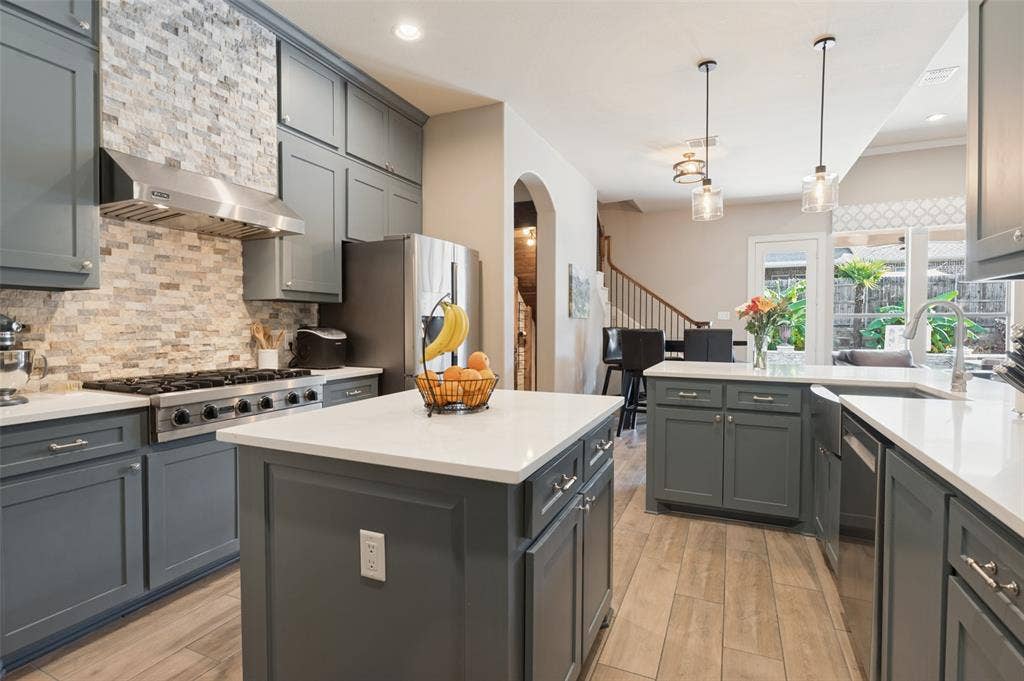 1504 Daisy Lane, Flower Mound, TX 75028 Kitchen featuring extensive cabinetry, stone backsplash, stainless steel range with hood, two islands with solid countertops, and wood-finish flooring