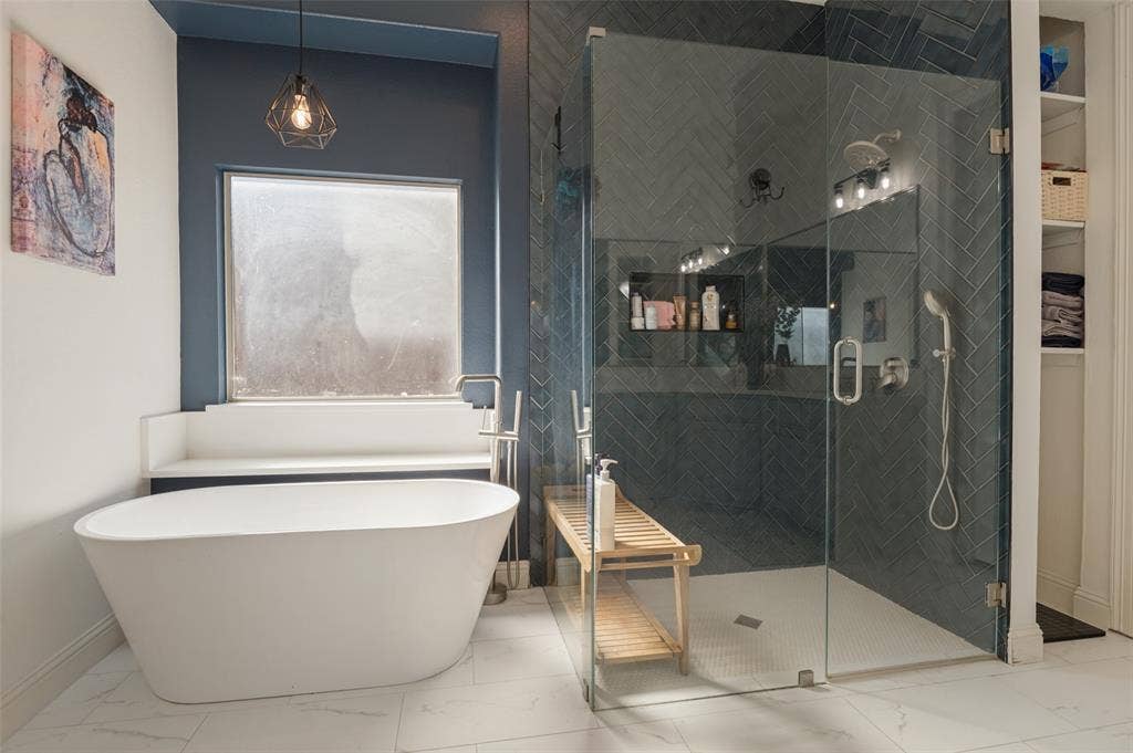 1504 Daisy Lane, Flower Mound, TX 75028 Freestanding soaking tub, glass-enclosed shower with herringbone tile, built-in shower niche, and white marble-look flooring