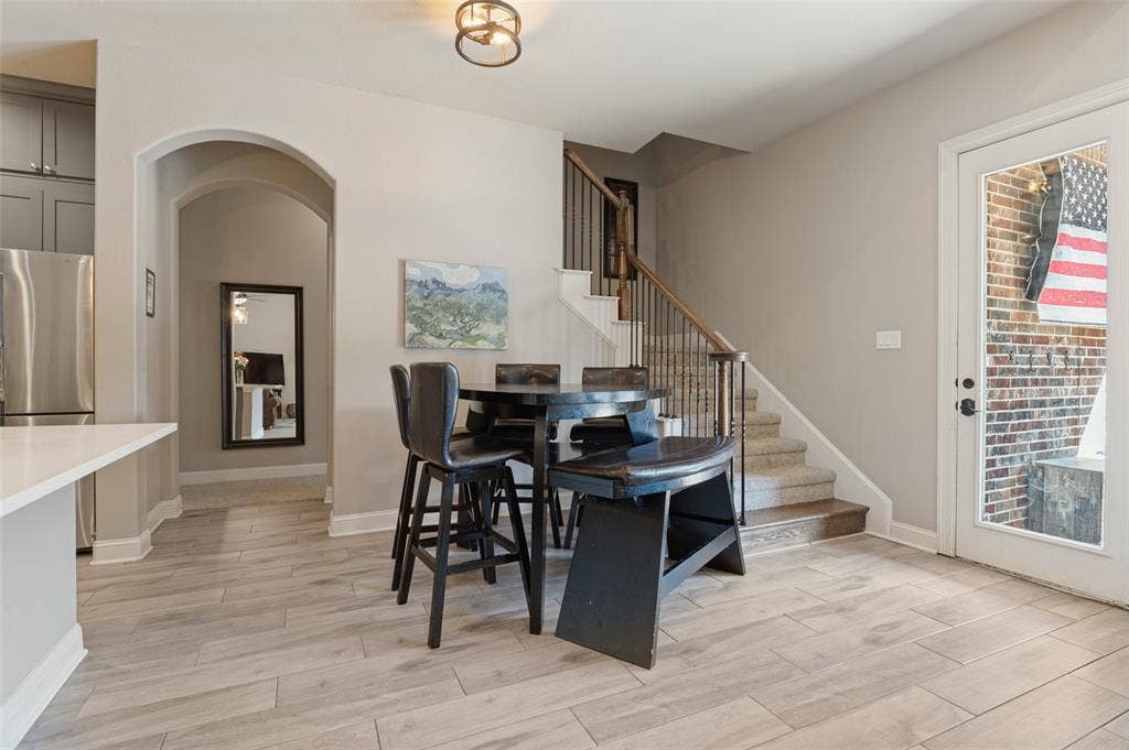 1504 Daisy Lane, Flower Mound, TX 75028 Wood-finish flooring throughout, arched doorway, stainless steel refrigerator, white quartz-like countertop, and staircase with metal spindles