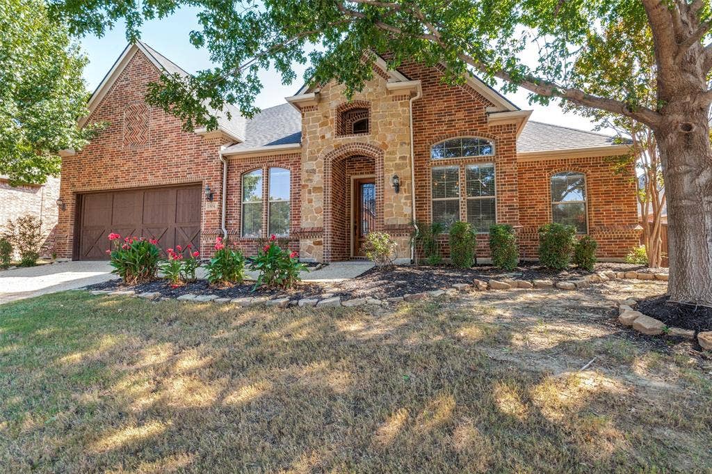 1504 Daisy Lane, Flower Mound, TX 75028 Brick and stone exterior with an arched entryway, decorative garage door, and well-maintained shrubbery