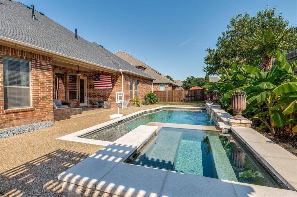 1504 Daisy Lane, Flower Mound, TX 75028 Brick exterior with a covered patio, exposed aggregate patio, and an in-ground swimming pool with an integrated spa