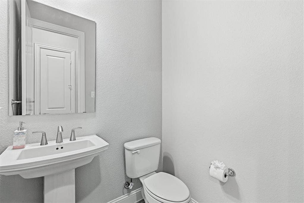 Pedestal sink with a polished chrome faucet, rectangular wall-mounted mirror, and a white toilet